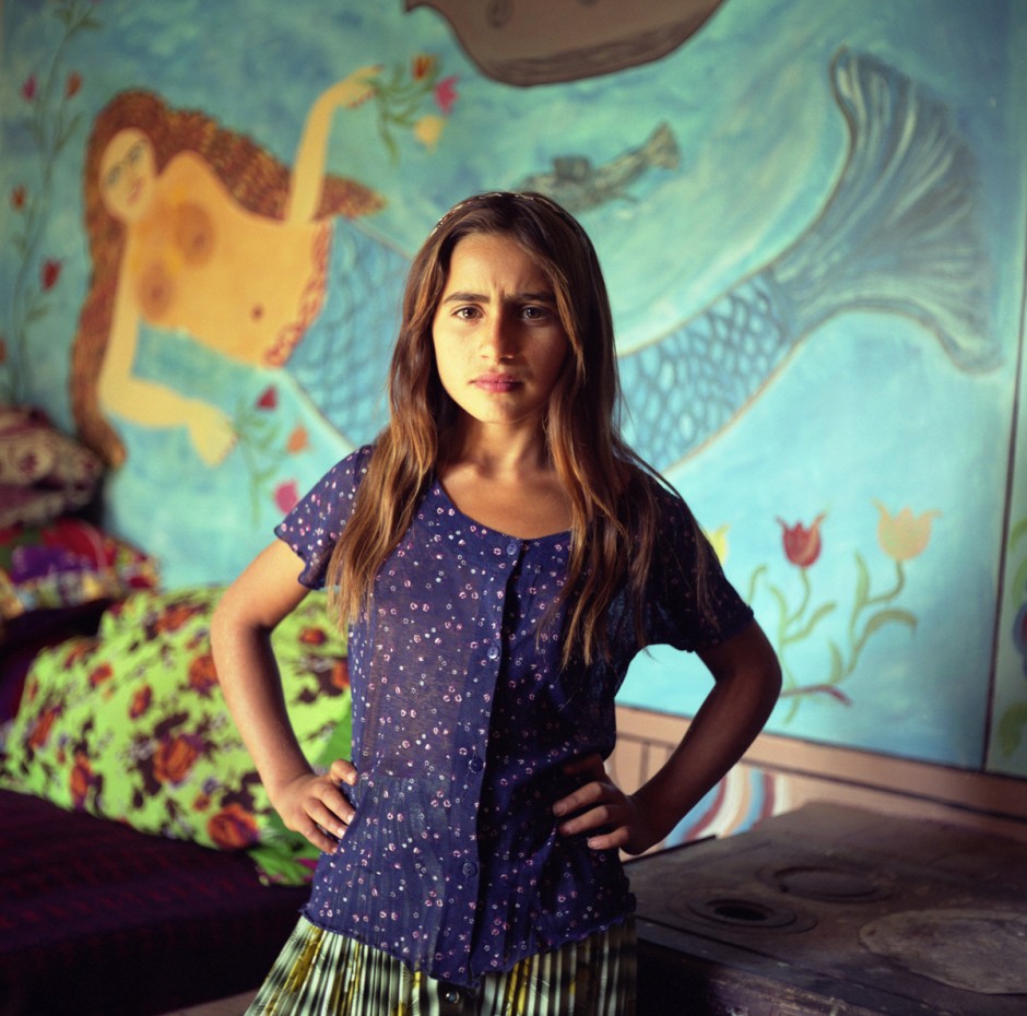 Mia, a young Roma girl stands in front of a mermaid painted on the wall of a Roma home, in the old part of the Roma camp of Sintesti.